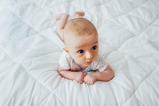 A small, smiling child, a boy, lies on a white bed and tries to crawl. 3, 4 months from the moment of birth. Photography, concept.