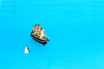 Fototapeta na wymiar the ship sails and next to it a fish jumps out of the water, creative minimal concept on a blue background, art creative design