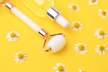 Serum with floral extracts for skincare, roller for face massage. Chamomile flowers on yellow background. Face and body care spa concept.
