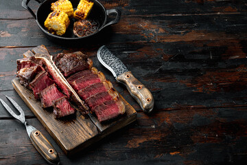 Grilled medium rare t bone or Porterhouse steak, on wooden serving board, on old dark  wooden table...