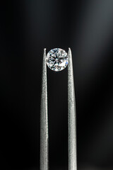 Round brilliant cut diamond with tweezers on black background