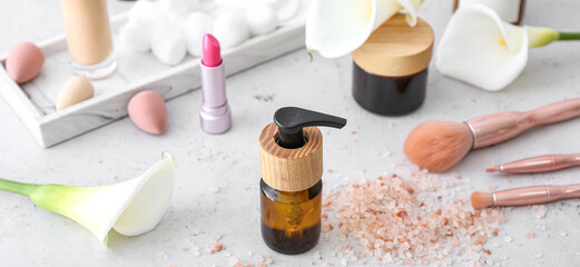 Different cosmetic products with makeup brushes, sea salt and calla lilies on light background