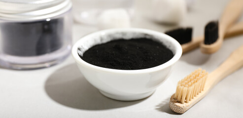 Bowl with activated charcoal tooth powder and brush on light background, closeup