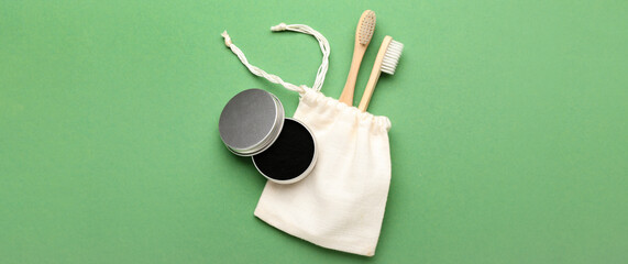 Jar with activated charcoal tooth powder and brushes on green background with space for text, top view