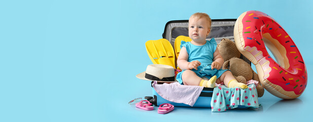 Adorable baby girl sitting in big suitcase with belongings on blue background with space for text