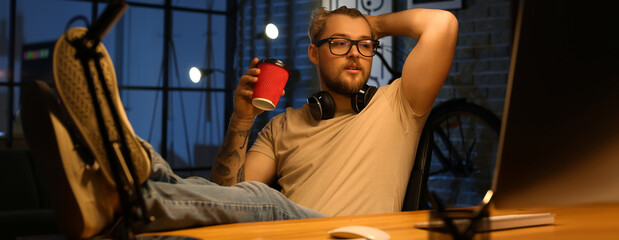 Young man drinking coffee while working at home late in evening