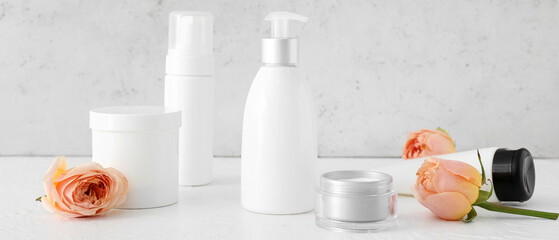 Different cosmetic products and beautiful rose flowers on light background