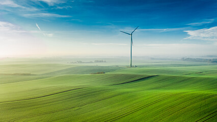 Foggy wind turbine on green field at sunrise