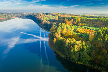 Forest and crystal clear lake with chemtrail reflection, aerial view