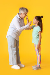 Little girl and her grandma touching each other's noses on yellow background
