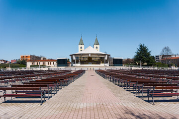 A Photograph of the exterior of the St. James church in Medjugorje with benches in the foreground
