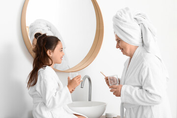 Little girl and her grandma with glasses of water in bathroom