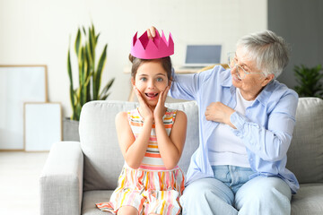 Surprised little girl with paper crown and her grandma at home