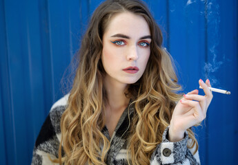 Beautiful girl smokes while waiting in the street.