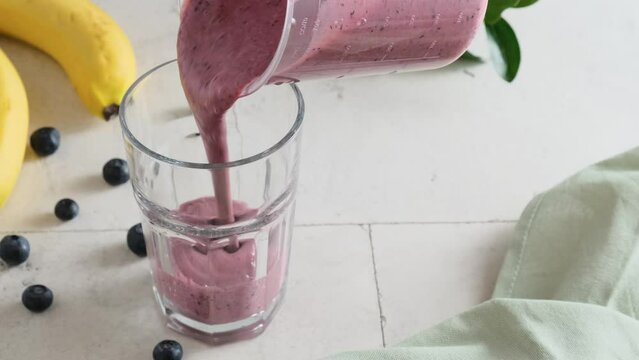 Pouring blueberry and banana smoothie in a glass. Summer refreshing fruit and berry drink. 4k video