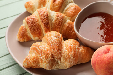 Plate of delicious croissants with peach jam on green wooden background, closeup
