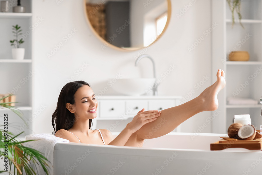 Wall mural Beautiful woman applying coconut oil onto her leg in bathroom