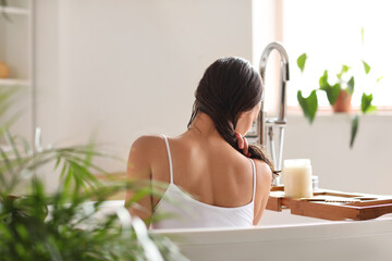 Young woman applying coconut oil onto her hair in bathroom