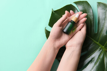 Female hands with bottle of natural serum and palm leaf on color background, closeup