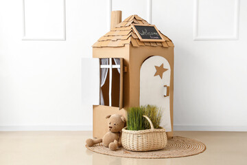 Toy cardboard house and basket with grass near light wall