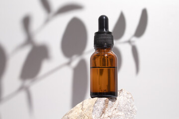 Cosmetic bottle serum, oil on stone stand with shadow branch eucalyptus on grey background. Natural...