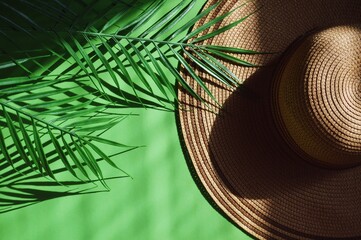 Spa luxury resort image. Summer sea travel concept. Palm leaves and straw hat in the sunlight in a green background. Flat lay fashion photography in minimalist style