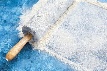 Rolling pin and wheat flour on color background, closeup