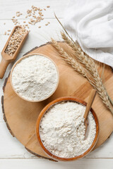 Bowls with wheat flour on board against white wooden background