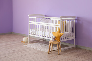 Baby crib, stool and basket with toys near violet wall