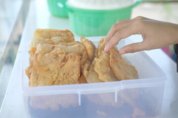 Close-up of a woman's hand taking a piece of fried tempeh