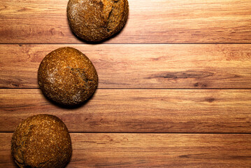 Homemade wholemeal loaves on a wooden table, breads arranged in line. Dark wood background, top view and space for text.