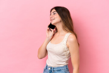 Young caucasian woman isolated on pink background keeping a conversation with the mobile phone with someone