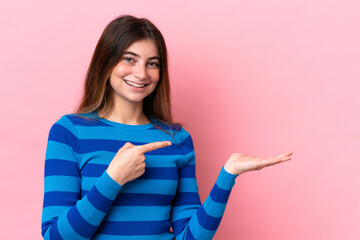 Young caucasian woman isolated on pink background holding copyspace imaginary on the palm to insert an ad