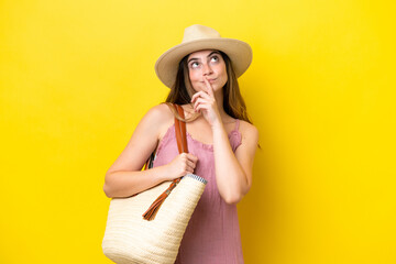 Young caucasian woman holding a beach bag isolated on yellow background having doubts while looking...