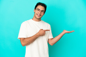 Caucasian handsome man over isolated blue background holding copyspace imaginary on the palm to...