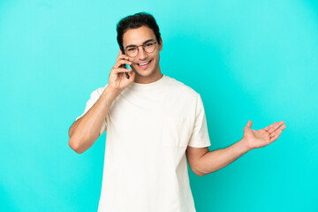 Caucasian handsome man over isolated blue background keeping a conversation with the mobile phone with someone