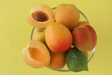 A transparent bowl full of apricot with green leaf isolated on yellow background. Cut fruit with detail. Top view and close up shooting.