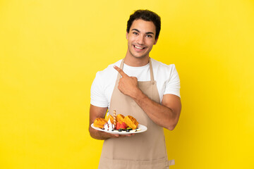 Restaurant waiter holding waffles over isolated yellow background pointing to the side to present a product