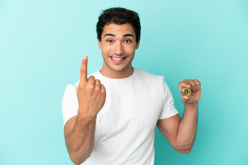 Naklejka premium Young man holding a Bitcoin over isolated blue background doing coming gesture