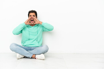 Caucasian handsome man sitting on the floor shouting and announcing something
