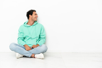 Caucasian handsome man sitting on the floor laughing in lateral position