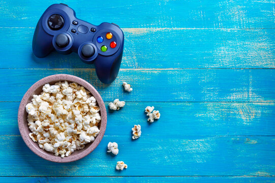 A bowl of popcorn and a game console on a blue wooden background with copy space. Top view. The concept of leisure, games, pastime.