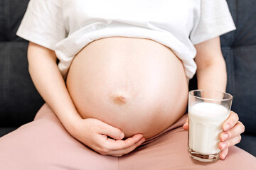 Pregnant young woman drinking milk while sitting on sofa at home