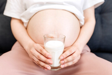 Pregnant young woman drinking milk while sitting on sofa at home