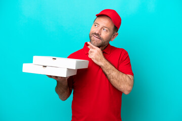 Pizza delivery man with work uniform picking up pizza boxes isolated on blue background looking up while smiling