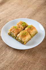 Pistachio baklava on a white plate.A plate baklava on fabric background
