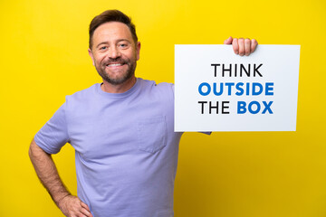 Middle age caucasian man isolated on yellow background holding a placard with text Think Outside...