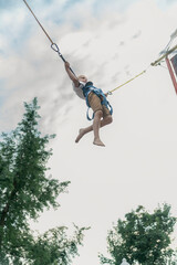 Little boy rides trampoline in an amusement park and jumps high into sky. Child has fun in the...