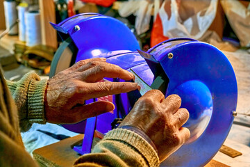 Hands of an elderly man sharpening a knife on a blue grinder