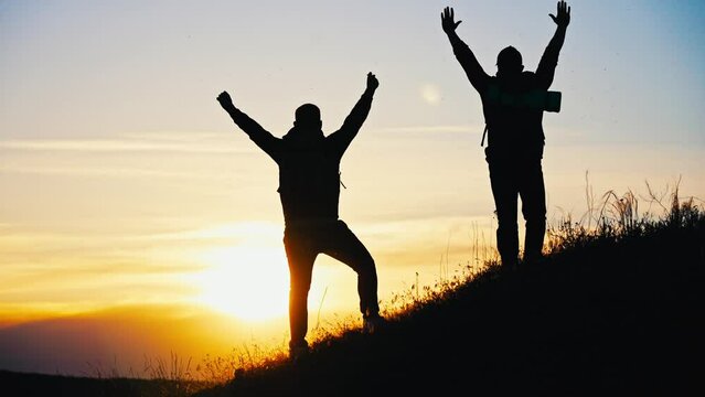 Silhouette tourists on hike with backpacks and equipment climbed on high mountain. Raise your hands up. Achieving set goal. Victory over yourself and great endurance and willpower. Sport lifestyle.